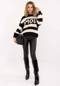 Schwarz-weiß gestreifter Pullover mit dem Schriftzug "AMOUR", kombiniert mit schwarzen Leggings aus Kunstleder und kniehohen glänzenden schwarzen Stiefeln.