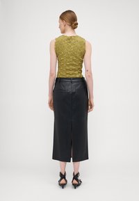 Maslinasto zeleni teksturirani top bez rukava u kombinaciji s crnom kožnom midi suknjom s stražnjim prorezom i elegantnim, minimalističkim dizajnom.