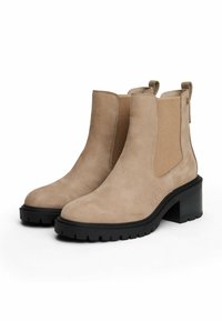 Bottes chelsea en suédine beige avec des panneaux élastiques sur les côtés, semelles épaisses noires et talons carrés, présentées sur un fond blanc.