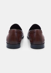 Ruskeat nahka loafersit, joissa on sileä pinta, matala korko ja pyöreä takapää. Musta sisäpohja ja kumipohja. Minimalistinen muotoilu ilman näkyviä yksityiskohtia.