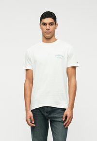 Tricou alb din bumbac, cu mâneci scurte, guler rotund și text brodat albastru pe față. Purtați cu blugi de un albastru închis.