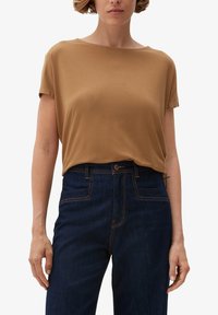 Brun kortærmet top med en løs pasform og en bred halsudskæring. Kombination med mørkeblå højtaljede jeans med synlige syninger.