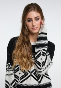 Svart och grått stickat tröja med geometriska mönster, långa ärmar och rund halsringning, med en mjuk, texturerad finish.