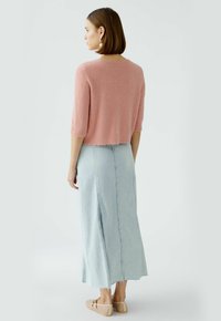 Helles rosa gekürztes Sweatshirt mit kurzen Ärmeln, kombiniert mit einem langen hellblauen Jeansrock mit einem vorderen Schlitz und fransigem Saum. Braune flache Schuhe.