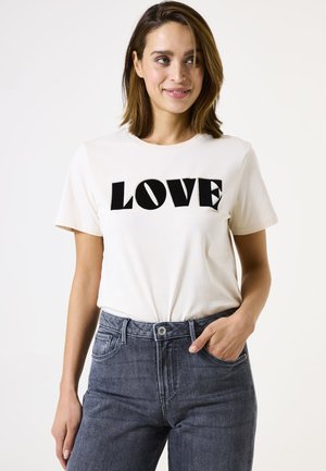 Crème-kleurig katoenen T-shirt met "LOVE" in vetgedrukte zwarte letters. Gepaard met donkergrijze denim jeans die een relaxte pasvorm en klassiek ontwerp tonen.