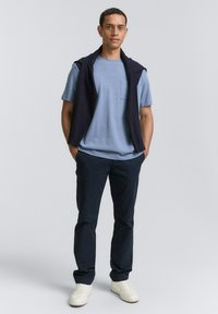 Camică scurtă, de culoare albastru deschis, cu un buzunar, asortată cu pantaloni navy și un veston închis la culoare pus pe umeri. Adidași albi completează look-ul.