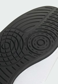 Rubber outsole with circular and linear tread patterns; smooth white upper material; overall rounded shape with a textured edge.