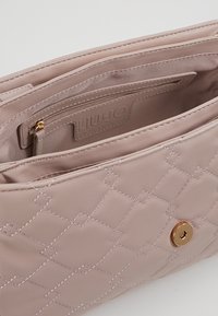 Lyserød lædertaske med quiltet mønster, der har en guld snapknaplukning og en lynlåslomme indeni.