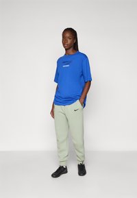 Blå oversized T-skjorte med 'LONDON'-grafikk, sammen med lysegrønne joggebukser med svart Nike-logo, og svarte sneakers.