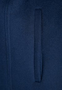 Mörkblå fleecetyg med en mjuk textur som har en vertikal ficka söm. Tyget har ett mjukt, borstat utseende.