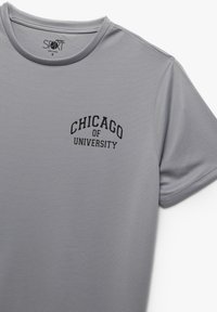 Grå trænings T-shirt med korte ærmer, med sort tekst der står "UNIVERSITETET I CHICAGO" på den øverste venstre side foran.