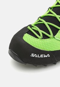 Baskets de sport vertes et noires avec une tige en mesh, un embout en caoutchouc et une semelle bien marquée, avec des lacets noirs et un logo blanc.