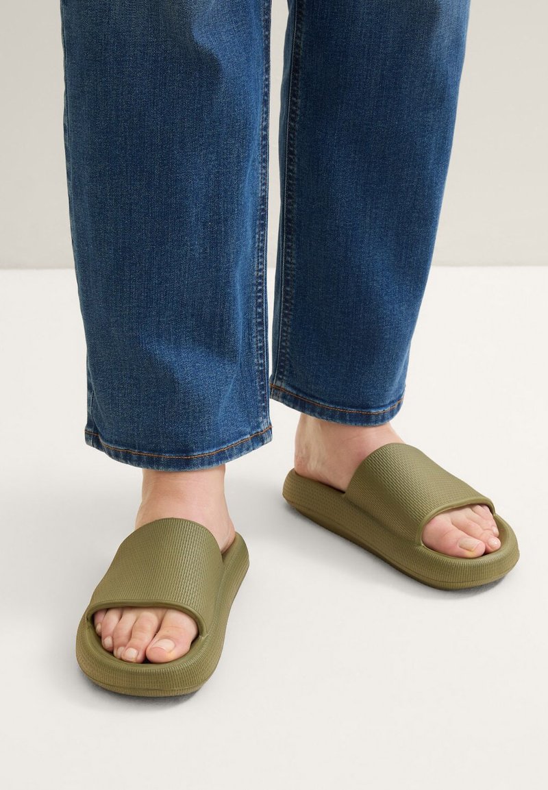 Sandales à glissière vert olive avec un dessus texturé, une large sangle et une semelle épaisse, associées à un jean en denim bleu légèrement ample.