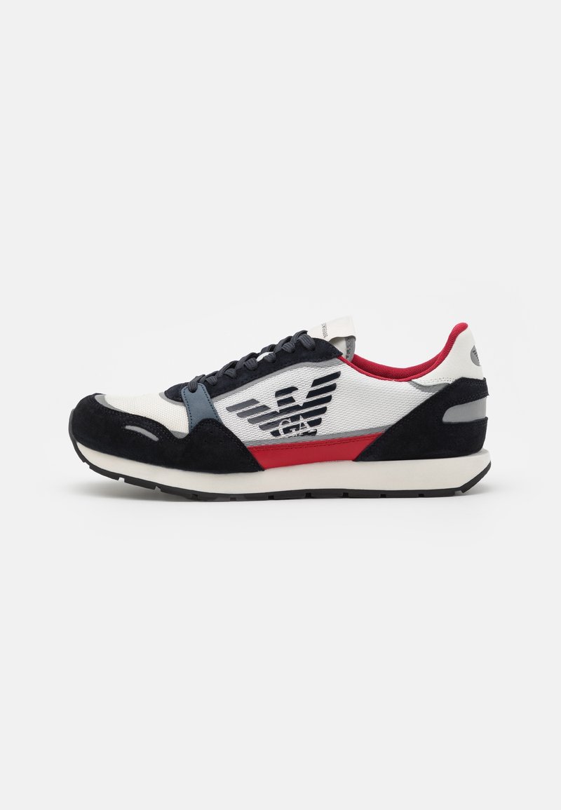 Baskets basses avec des panneaux noirs, blancs, rouges et gris, lacets noirs, intérieur rouge, et un logo aigle noir avec des lettres sur le côté.