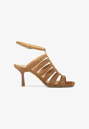 Sandale à talon haut en daim marron clair avec des brides découpées et une bride à boucle à la cheville, avec un talon fin et effilé sur fond blanc.