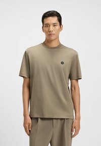 T-shirt a maniche corte, con scollatura a girocollo in tessuto verde oliva, con un piccolo logo nero sul lato sinistro del petto e una vestibilità comoda.