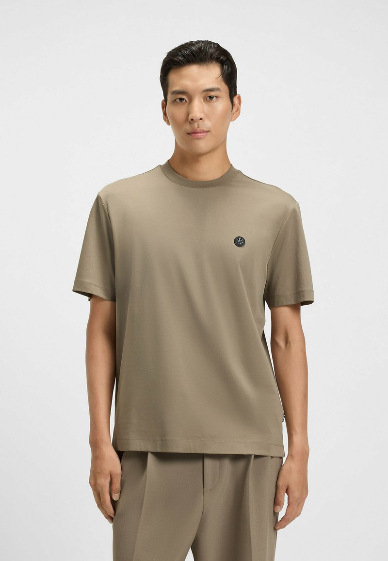 T-shirt a maniche corte, con scollatura a girocollo in tessuto verde oliva, con un piccolo logo nero sul lato sinistro del petto e una vestibilità comoda.