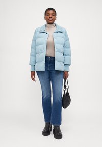 Chaqueta acolchada de color azul claro, suéter de cuello alto gris, jeans de campana azules, botas de plataforma negras y bolso pequeño negro. Textura suave y diseño acolchado.