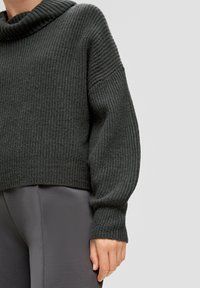 Ciemnoszary sweter wykonany na drutach z prążkowanej tekstury, z dekoltem w kształcie łódki i opadającymi ramionami. W zestawie z szarymi, dopasowanymi legginsami.