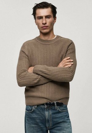 Brun ribbad stickad tröja med rundad hals, ihopparad med blå jeans. Texturen är tjock och mysig, med en åtsittande design.