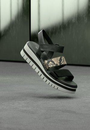Sandale negre cu platformă, cu o curea texturată cu imprimeu de șarpe, având accente din piele netedă și o talpă groasă albă cu caneluri.