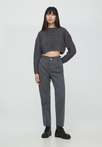 Maglione corto grigio a maglia con motivo a treccia, abbinato a pantaloni grigi a vita alta e stivaletti neri con lacci. Design semplice e moderno.