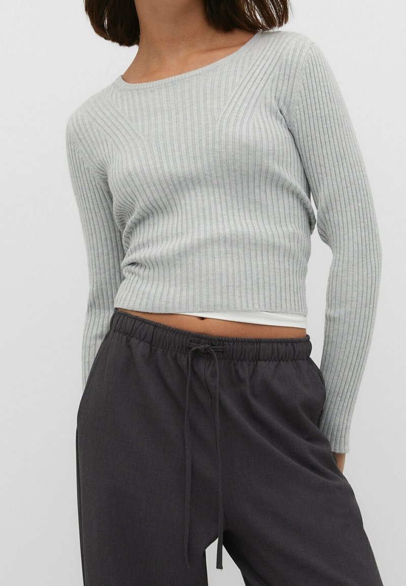 Graues, geripptes, langärmeliges Crop-Top mit figurbetontem Design und rundem Ausschnitt. Kombiniert mit dunklen, lockeren Hose mit Kordelzug.