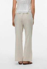Lichtbeige, wijde broek gemaakt van een gestructureerde stof, met een subtiele glans en een losse pasvorm, gecombineerd met een paar bruine sandalen.