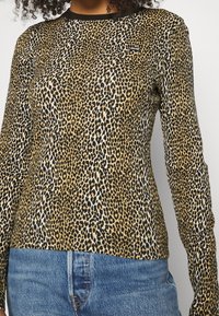 Långärmad leopardmönstrad topp med svart halsringning, tillverkad av mjukt material; har en figurnära design och framträdande djurmönster.