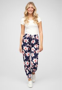 Pantaloni jogger blu navy con stampa floreale in bianco e rosa, vita elastica e polsini arricciati, abbinati a una t-shirt bianca semplice e scarpe bianche.