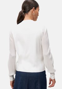 Pull blanc avec un corps ajusté et des manches bouffantes plissées texturées. Encolure ronde et poignets côtelés. La vue de dos montre une finition en tissu lisse.