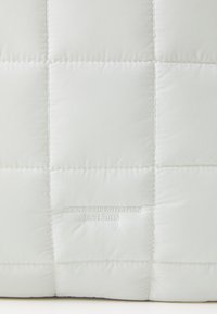 Matériau blanc matelassé avec un motif en grille, comportant un texte en relief "ARKK COPENHAGEN EST. 2015" en bas. Texture douce et lisse.
