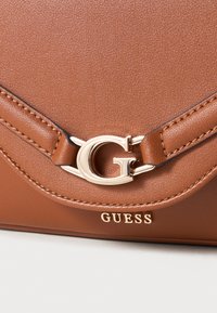 Brown faux leather handbag featuring a gold-tone logo clasp and stitching details; presents a smooth texture and structured design.