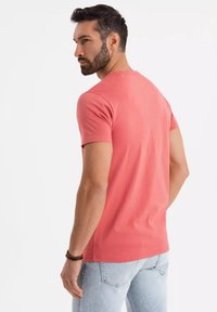 Korálově růžové tričko s krátkým rukávem, bavlněná tkanina, klasický kulatý výstřih, slim fit, nošeno s světle modrými džíny, jednoduché švy, hladký zadní díl.