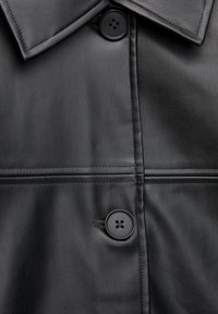 Czarna skórzana kurtka z wyrazistym kołnierzem, dwoma czarnymi guzikami i kontrastowymi przeszyciami. Gładka tekstura z dopasowanym krojem.