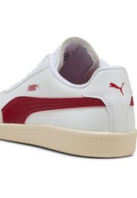 Weiße Ledersneaker mit rotem Wildleder-Seitenstreifen, Gummisohle und PUMA-Logo an der Ferse. Gepolsterter Kragen für zusätzlichen Komfort.