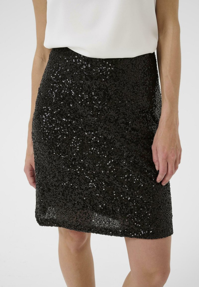 Falda negra con lentejuelas de diseño ajustado y superficie texturizada. Longitud corta y dobladillo limpio, combinada con una camiseta blanca simple.