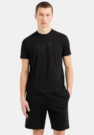 T-shirt nera in cotone con logo EA7 in rilievo, abbinata a pantaloni corti neri con logo stampato. Entrambi hanno una vestibilità semplice e rilassata.
