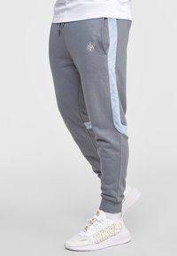 Graue Jogginghosen mit hellblauen seitlichen Streifen und weißen Logodetails. Mit elastischem Bund und Bündchen, aus glattem Stoff gefertigt.