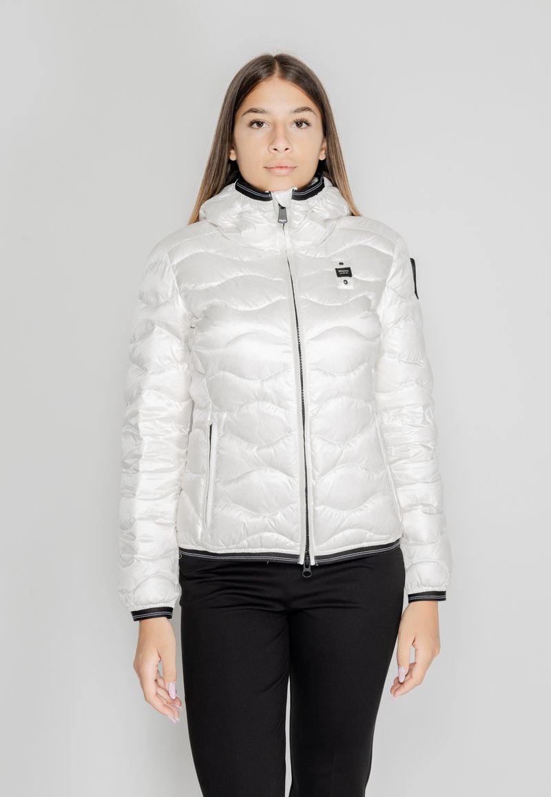 Giacca puffer bianca con texture trapuntata, collo alto e zip frontale. Presenta accenti neri sul collo e sui polsini.