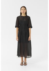 Black sheer midi dress with short sleeves, button front, gathered waist, and flowing silhouette. Worn over a black outfit, paired with sandals.