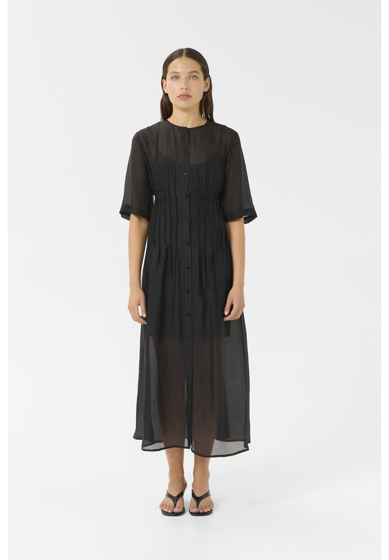 Black sheer midi dress with short sleeves, button front, gathered waist, and flowing silhouette. Worn over a black outfit, paired with sandals.