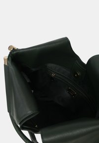 Borsa a tracolla verde in pelle con finitura testurizzata, dotata di tasca con zip, accessori in oro e un ampio interno nero.