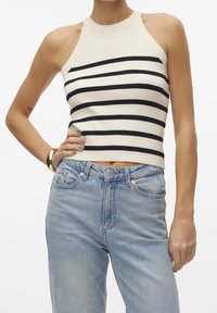 Top corto acanalado a rayas en crema y azul marino, con un cuello alto y diseño sin mangas, combinado con unos vaqueros de tiro alto en azul claro.