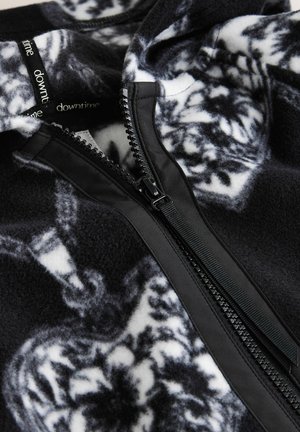 Fleece pullover in black and white with intricate patterns. Features a contrasting black zipper and soft, textured fabric.