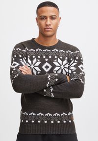 Dark green knitted sweater with white and gray fair isle patterns, crew neck, and ribbed cuffs. Features a small logo at the hem.