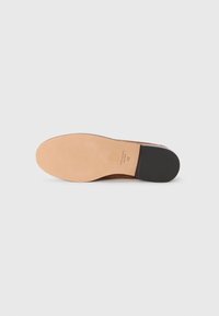 Brūnas ādas kurpes zole ar melnu papēdi un "kate spade NEW YORK 6.5" izdrukātu uz iedeguma zoles uz baltas fona.