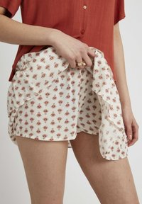 Shorts blancs à motifs rouges, fabriqués dans un tissu léger. Associés à un haut couleur rouille, présentant un design superposé décontracté.