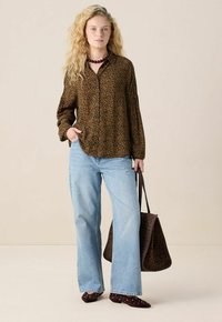 Blouse à imprimé léopard marron, jeans large bleu clair, ballerines bordeaux à clous, et sac à imprimé léopard marron. Tissu texturé et coupe décontractée.