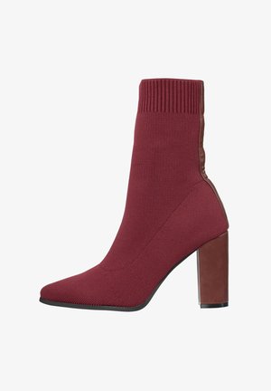 Bottine bordeaux avec une tige en maille, un bout pointu et un talon bloc haut. Comprend des accents marron lisses au talon et sur le côté.